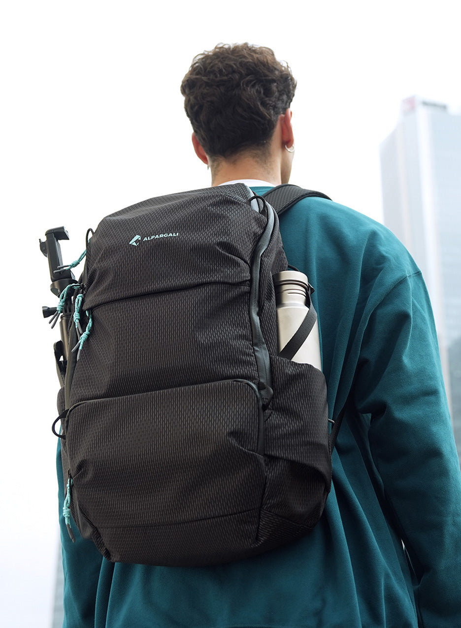 Person wearing a black backpack with visible brand logo, standing against a light background.