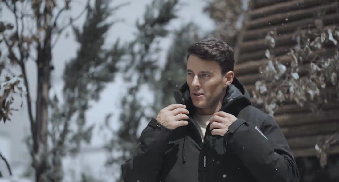 A man is adjusting his aerogel-insulated jacket in a snowy outdoor setting, showcasing its warmth and style.